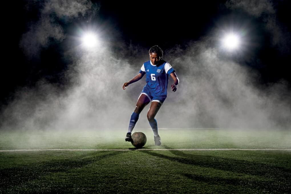 Darline Radamaker dribbles a soccer ball in a dramatically lit soccer field